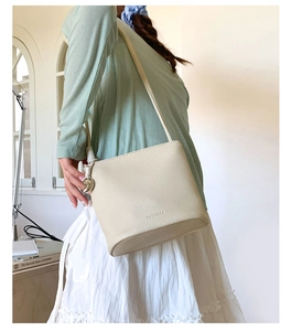 Détail du sac seau beige avec texture litchi et pendentif en forme de cœur argenté