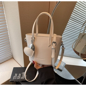 Detailed view of white litchi leather bucket bag featuring silver hardware and heart charm