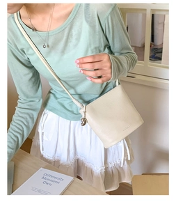 Détail d'un sac seau en cuir beige avec breloque cœur argentée et fine bandoulière