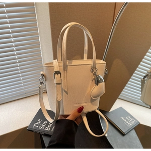 Detail of white lychee leather bucket bag with heart pendant on a wooden table