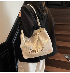 Detail of straw woven tote bag featuring Summer embroidery and a pearl lace charm