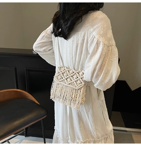 Detail of handmade cream crochet crossbody bag with long tassels on a white dress