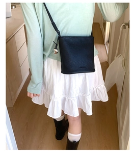 Détail d'un sac seau en cuir grainé noir avec une breloque en métal et une bandoulière