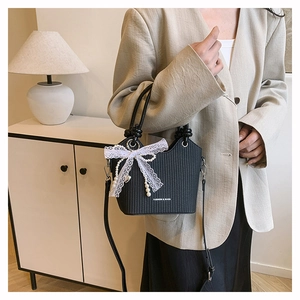 Détail du sac seau noir avec nœud en dentelle blanche, perle et texte de mode