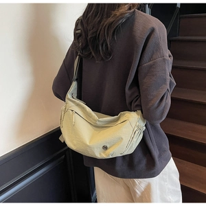 Close-up of light green nylon crescent crossbody bag with pleated sides and zip pocket
