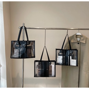 Detail view of transparent and frosted PVC tote bags with black handles hanging on a rack
