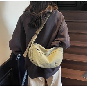 Detail of avocado green nylon crescent crossbody bag worn over a dark brown hoodie