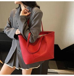 Detail of red pebbled leather tote bag with dual straps worn by model in urban setting