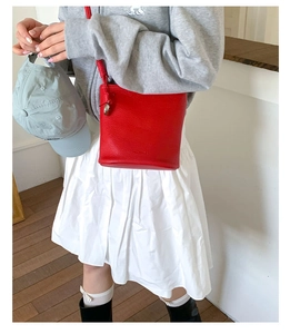Détail du sac seau rouge texturé litchi avec pendentif argenté porté par le modèle