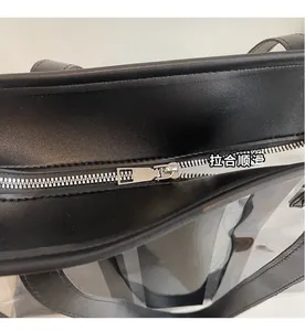 Detailed macro view of the smooth silver metal zipper and black leather trim on a PVC tote