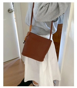 Détail d'un sac seau en cuir marron texturé avec fine bandoulière et nœud décoratif