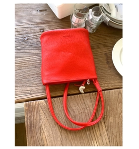 Gros plan du sac seau en cuir grainé rouge avec pendentif cœur argenté et bandoulière