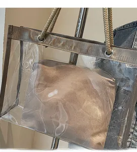 Detail of transparent PVC tote bag featuring golden ribbon trim and woven rope handles