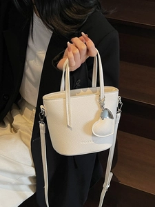 White pebbled leather bucket bag with top handle and heart charm on a wooden staircase
