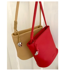 Détail de sacs seaux en cuir grainé rouge et kaki avec breloques cœur et bandoulières