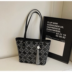 Dettaglio della borsa tote nera con motivo geometrico bianco e nappa grigia appesa