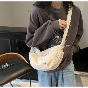 Detail view of a beige crescent canvas crossbody bag worn by a model in a minimalist setting