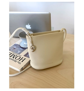 Détail du sac seau crème montrant le charme de coeur argenté et la bandoulière nouée
