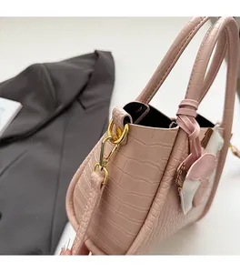 Dettaglio borsa a mano rosa con trama a coccodrillo, fibbia dorata e ciondolo ad ala