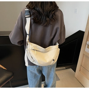 Close-up of beige crossbody bag with wide canvas strap and black buckle closure