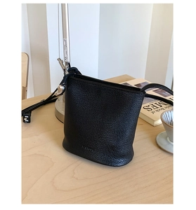 Détail du sac seau noir en cuir grainé avec texte Father embossé sur une table en bois