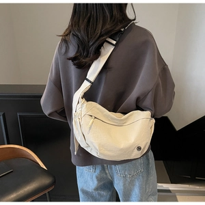 Detailed view of the wide shoulder strap and natural pleats on a beige nylon crossbody bag