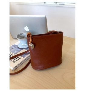 Détail du sac seau marron caramel avec cuir à texture litchi et breloque en métal