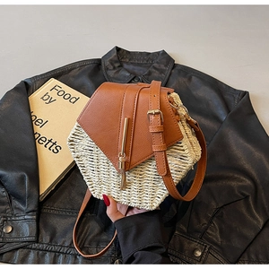 Detail of a hexagonal straw bag with brown leather flap, gold metal bar, and tassel accent