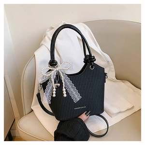Détail d'un sac seau noir tissé avec nœud en dentelle et pendentif en perles élégant
