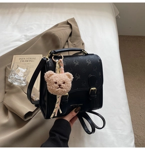 Detail eines schwarzen Lederrucksacks mit goldenen Schnallen und einem süßen Bärenanhänger
