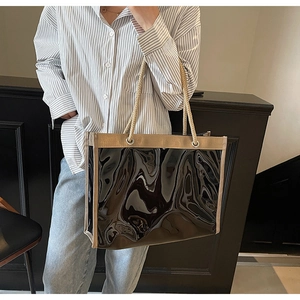 Detail of glossy black tote bag featuring beige fabric trim and woven rope handles