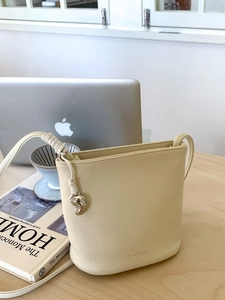Sac seau minimaliste en cuir crème avec breloque argentée sur un bureau en bois