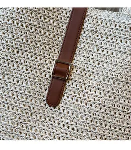 Detail of woven straw tote bag with brown leather strap and silver metal buckle