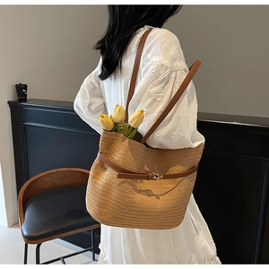 Détail d'un sac cabas en paille avec lanières en cuir marron sur une robe blanche brodée