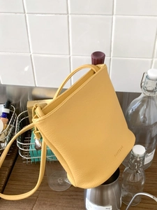 Sac seau minimaliste en cuir jaune vif avec bandoulière dans un décor élégant et chaleureux
