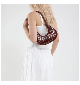 Détail du sac croissant bordeaux à clous argentés porté sur une robe blanche