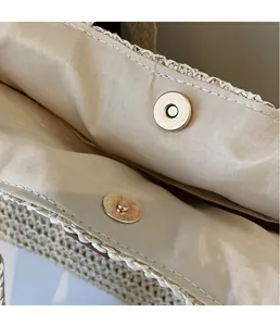 Detail of light gold magnetic clasp closure on a woven straw tote bag with beige lining