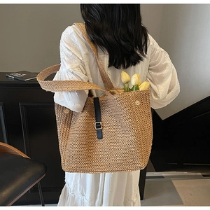 Close-up of woven straw tote bag with black leather strap buckle and yellow tulips