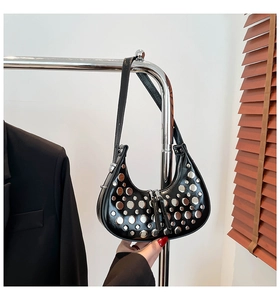 Détail d'un sac hobo noir en cuir avec clous argentés et fermeture éclair sur un support mural