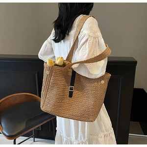 Detail of hand-woven straw tote with black strap, metal buckle and yellow tulip accents