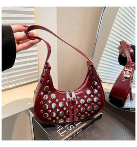 Détail d'un sac demi-lune bordeaux avec clous argentés sur livre et reflet miroir