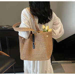 Close-up of handmade woven straw tote bag with black leather buckle strap detail