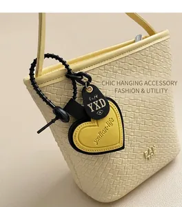 Gros plan du sac seau tissé jaune avec un charm coeur contrasté et logo de marque YXD