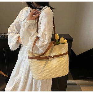 Détail du sac cabas en paille avec lanières en cuir marron et boucle sur robe blanche
