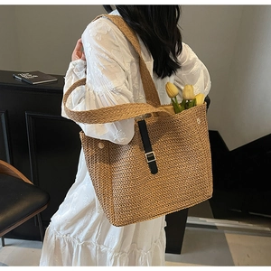 Close-up of a large straw tote bag with black leather buckle and shoulder strap