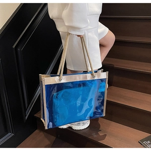 Blue transparent PVC tote bag detail with beige rope handles and inner pouch on stairs