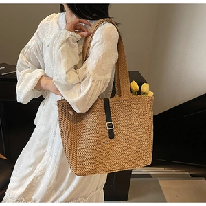 Detail of woven straw tote bag featuring black leather strap and golden buckle closure