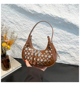 Close-up of brown crescent underarm bag with silver round rivets on glossy leather