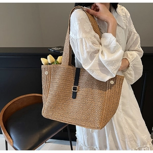 Detail of woven straw tote bag with black leather strap and golden metal buckle