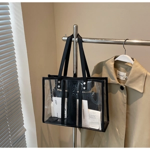 Détail du sac cabas en PVC transparent avec poignées en cuir noir sur un porte-manteau